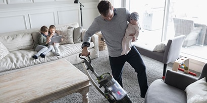 a man vacuuming with a baby in his arms