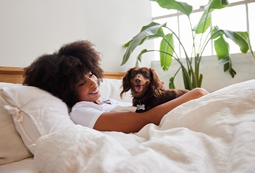 A woman smiling in bed with her dog.