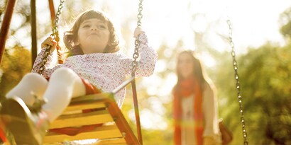 A woman pushing a child on a swing on a sunny day.
