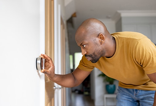 Introduce smart gadgets in your home to save time and money. A man using a smart thermostat.