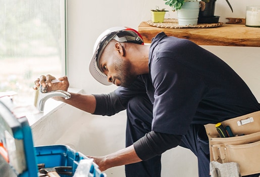 Discovering potential problems in your older home can be overwhelming, but fear not! We’ve got you covered with tips on managing them effectively. A man fixing a faucet in a brightly lit space.