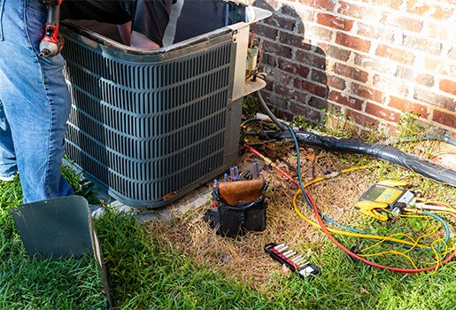 An outdoor air conditioning condenser is undergoing maintenance with the access panel and top cover removed.