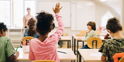A classroom of young students, one raising their hand.
