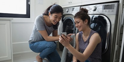 two women looking at a phone screen in front of a washer and dryer
