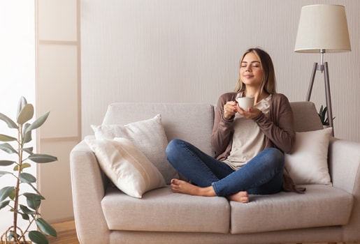 Woman sitting on a couch, holding a mug with eyes closed, enjoying a relaxed moment.