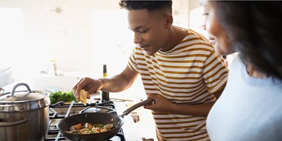 A man and woman cooking a dish on the stove.
