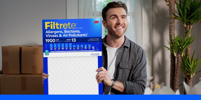 A man holding a Filtrete MPR 1900 Air Filter in a living room.

