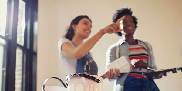Two women discussing paint colors, with paint cans in the foreground.
