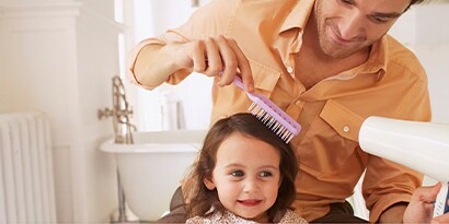 A Father brushing and blow drying his daughter’s hair.
