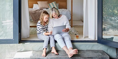 A Woman and child sit and look at a tablet together in a doorway.
