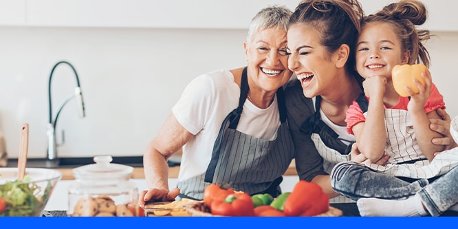 A family smiling cooking together in a kitchen, with bell peppers in a basket in the foreground
