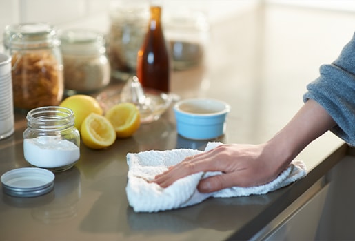 Everything you need to treat tough stains, eliminate odors and remove burnt-on food particles is likely already in your pantry. A person wiping down a surface with lemons and baking soda in the background.