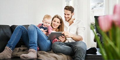 A two adults and a baby on a couch with a tablet.
