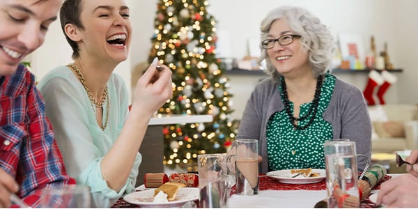 Two people smiling in a festively decorated dining room. A Christmas tree in the background.
