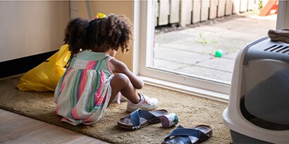 A young girl sitting on a doormat putting her shoes on.
