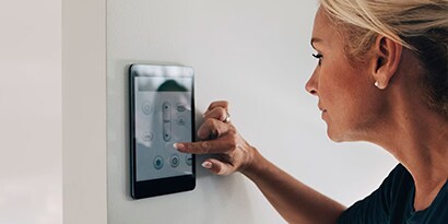 A woman using a smart thermostat on a wall.
