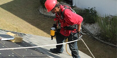 A man on the roof of a house doing roofing work.
