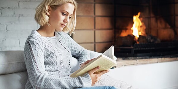 Woman reading a book in front of a fireplace.
