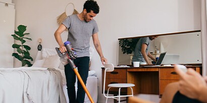 A man vacuuming a bedroom.
