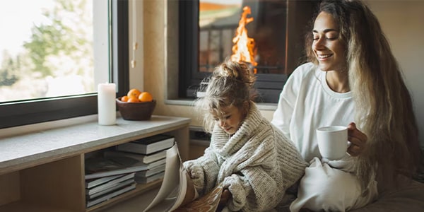 A mother and daughter sit in front of a fireplace reading a book.
