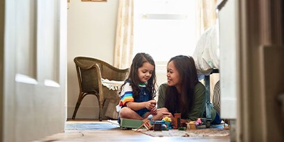 A woman playing with toys on the floor with a young child.

