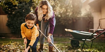 A Mother and son raking leaves in a backyard.
