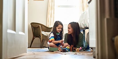 A woman playing with toys on the floor with a young child.
