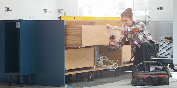 Person assembling kitchen cabinets with a drill, surrounded by construction tools.
