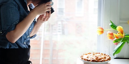 a person photographing a pie next to a vase of tulips