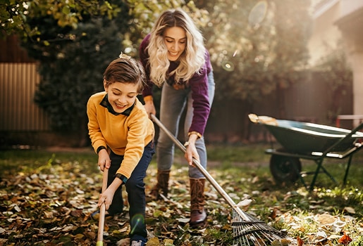 We’re answering your top questions about fall allergy season. A woman and son racking leaves in their backyard. A wheelbarrow is in the background.
