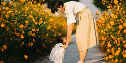 a woman and child holding hands in a field of flowers.