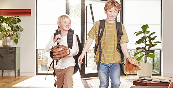 2 young boys running into their home with backpacks on
