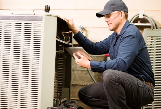 Technician in uniform using a tablet while inspecting an HVAC unit outdoors.