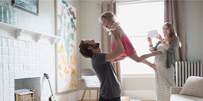 A father tossing a child in the air, with a mother taking a photo behind them.
