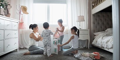 A family of four playing with a doll house in a bedroom.
