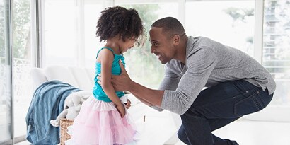 A man holding his daughter smiling in a brightly lit room.
