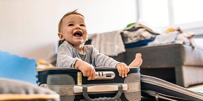 A toddler sitting in a suitcase, laughing.
