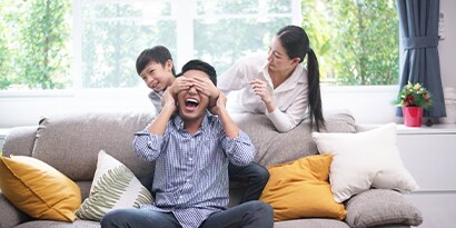 A family playing peekaboo with their child on a couch.
