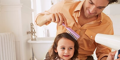 Father brushing and drying daughters hair with a hair dryer