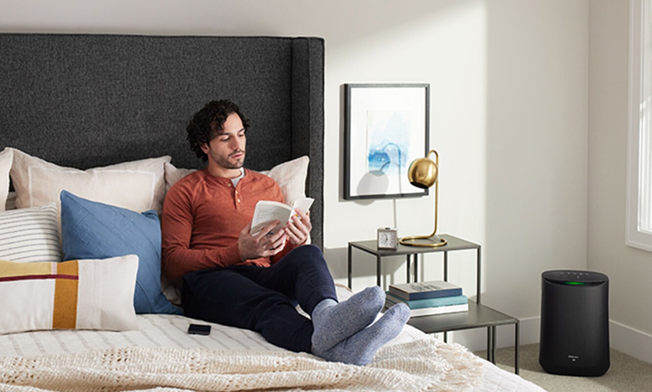 Man reading a book in bedroom with a Filtrete™ Smart Air Purifier
