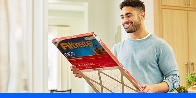 A man wearing a light blue pullover smiling and looking at a Filtrete MPR 1000 Air Filter.
