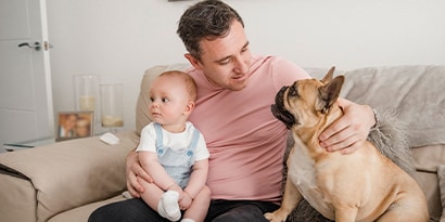 Man sitting on a couch with a dog and baby