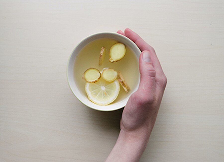 Hand Holding White Mug of Water with Lemon and Ginger
