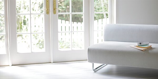 Minimalist living room with a white sofa near large glass doors. Books and a remote rest on the sofa.
