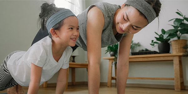 A woman and daughter exercise on the floor together smiling.

