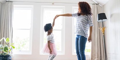A mother and daughter holding hands dancing in a bright living room.

