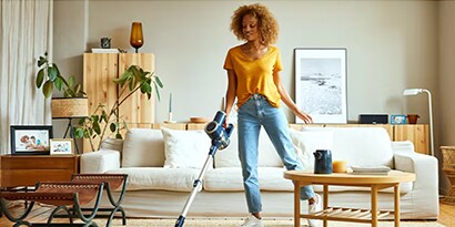 A woman vacuuming a living room, brightly lit.
