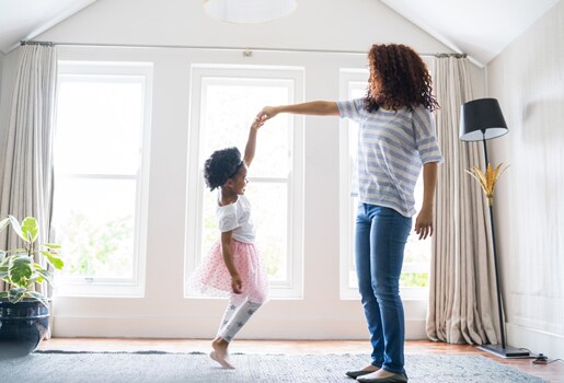 Mother and daughter doing ballet at home. Full length of happy girl and woman are performing dance together. Females are dancing against windows.