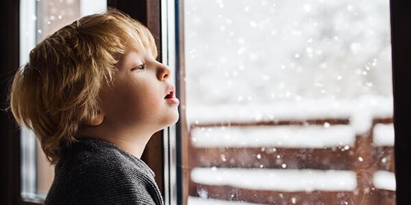 A kid looking out the window to snow outside.
